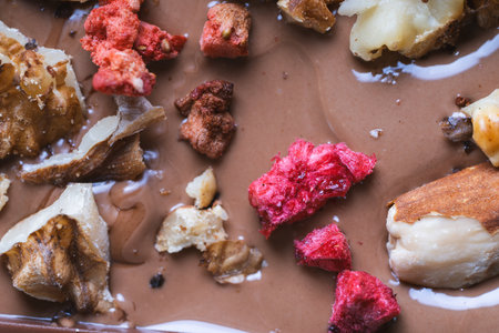 The process of making homemade chocolate. Nuts, freeze-dried raspberries and strawberries are laid out on liquid chocolate. High quality photoの写真素材