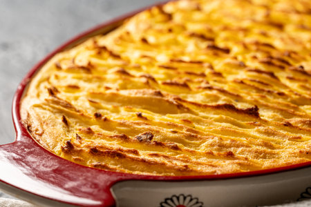 Potato casserole in a porcelain, red baking dish with a white towel on a gray background. Close-up. High quality photoの写真素材