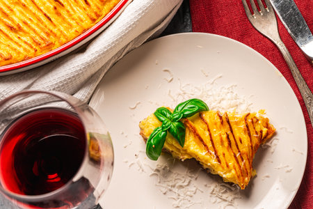 Mashed potato and minced meat casserole in a baking dish and a piece of casserole on a white plate with a burgundy napkin and cutlery on a gray background with a glass of red wine. High quality photoの写真素材