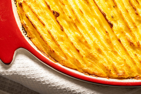 Potato casserole in a porcelain, red baking dish with a white towel on a gray background. Close-up. High quality photoの写真素材