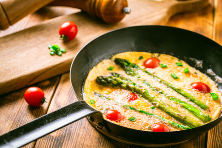 Omelet with tomatoes and asparagus in a pan on a wooden table. Delicious and healthy breakfast. High quality photoの写真素材