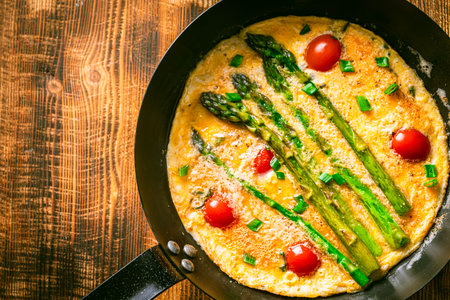 Asparagus with scrambled eggs and cherry tomatoes in a pan on a wooden background. View from above. Space for text. High quality photoの写真素材