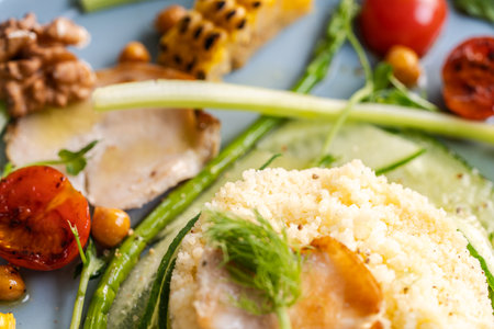 Couscous with chicken pieces, cucumbers, asparagus and corn, tomatoes and walnuts on a blue plate on a light background. Close-up. High quality photoの写真素材