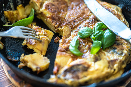 Traditional Spanish breakfast potato tortilla in a cast iron pan. Cut into pieces with a knife and...