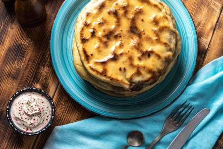 Traditional Caucasian, Eastern dish. Flatbread stuffed with minced meat with sauce on a turquoise plate with cutlery and a napkin on a wooden table. Top view. High quality photoの写真素材