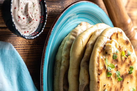 Khychins, traditional Caucasian, Eastern dish. Flatbread stuffed with minced meat with sauce on a turquoise plate with cutlery and a napkin on a wooden table. Vertical photo. High quality photoの写真素材
