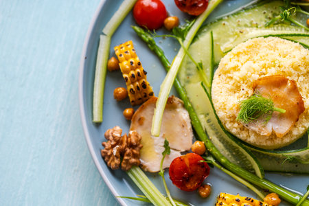 Couscous with chicken pieces, cucumbers, asparagus and corn, tomatoes and walnuts on a blue plate on a light background. Close-up. High quality photoの写真素材