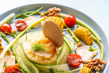 Couscous with chicken pieces, asparagus and corn, tomatoes and walnuts on a blue plate on a light background. Close-up. High quality photoの写真素材