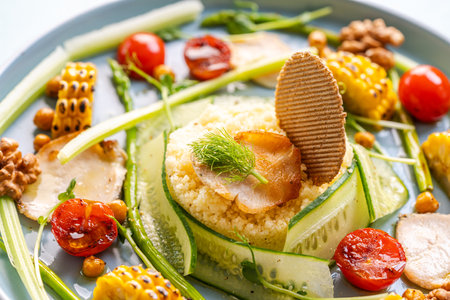 Couscous with chicken pieces, cucumbers, asparagus and corn, tomatoes and walnuts on a blue plate on a light background. Close-up. High quality photoの写真素材