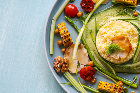 Couscous with chicken pieces, cucumbers, asparagus and corn, tomatoes and walnuts on a blue plate on a light background. Copyspace. High quality photoの写真素材