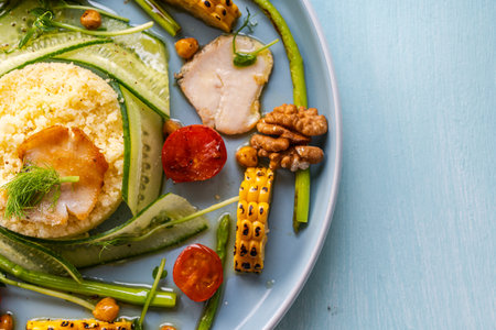 Couscous with chicken pieces, cucumbers, asparagus and corn, tomatoes and walnuts on a blue plate on a light background. Copyspace. High quality photoの写真素材