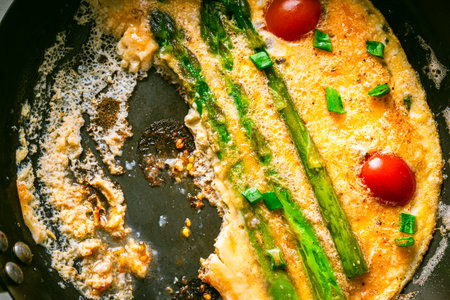 Omelet with asparagus and tomatoes in a cast-iron pan, half of the dish is eaten. Close-up. High quality photoの写真素材