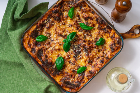 Lasagna in a baking dish according to a traditional Italian recipe on a white table with a green napkin and spices. View from above. Copyspace. High quality photoの写真素材