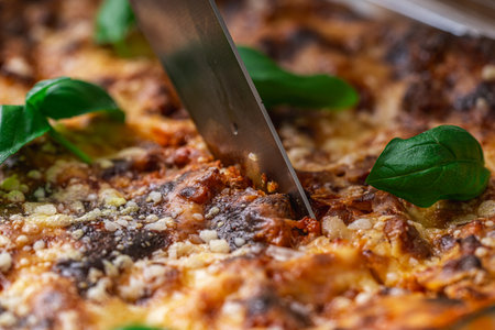 Lasagna in a baking dish according to a traditional Italian recipe is cut with a knife. Close-up. High quality photoの写真素材