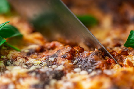 Lasagna in a baking dish according to a traditional Italian recipe is cut with a knife. Close-up. High quality photoの写真素材