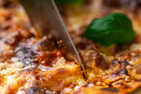 Lasagna in a baking dish according to a traditional Italian recipe is cut with a knife. Close-up....