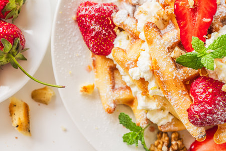 Belgian waffles with cottage cheese cream, strawberries, walnuts and mint on a white plate on a light table with a cup of coffee. Delicious, Sunday breakfast. Top view. High quality photoの写真素材