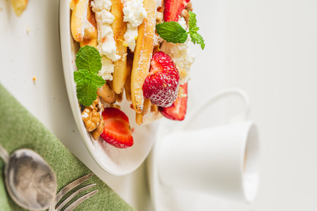 Belgian waffles with cottage cheese cream, strawberries, walnuts and mint on a white plate on a light table with a cup of coffee. Delicious, Sunday breakfast. High quality photoの写真素材
