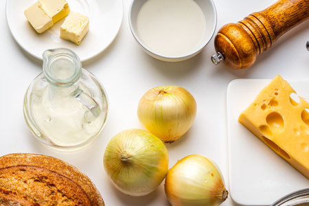 Ingredients for French onion soup. On the white table there is cheese, onions, bread, broth, mills...