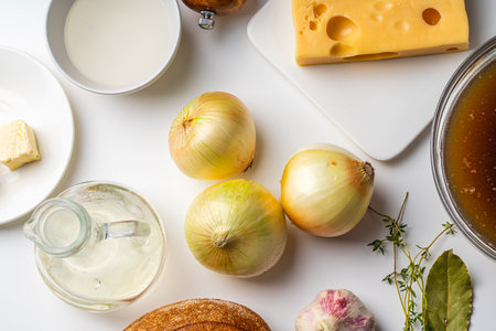 Ingredients for French onion soup. On the white table there is cheese, onions, bread, broth, mills with salt and pepper. Top view. High quality photoの写真素材