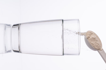Collagen powder is poured with a measuring spoon into a glass of water on a white background with a reflection. The medicine is diluted in water. Vertical photo. High quality photoの写真素材