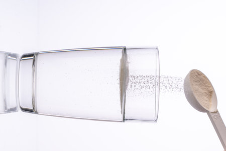 Collagen powder is poured with a measuring spoon into a glass of water on a white background with a reflection. The medicine is diluted in water. Vertical photo. High quality photoの写真素材