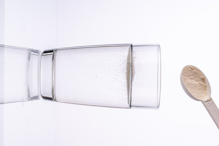 Collagen powder is poured with a measuring spoon into a glass of water on a white background with a reflection. The medicine is diluted in water. Vertical photo. High quality photoの写真素材