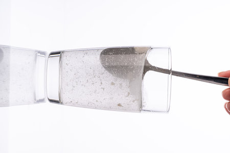 Collagen or medicinal powder is stirred with a spoon in a glass of water on a white background. High quality photoの写真素材