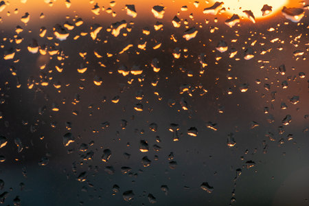 Raindrops on the window against the background of the setting sun. Background with glass and drip texture. High quality photoの写真素材