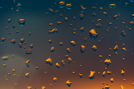 Raindrops on the window against the background of the setting sun. Background with glass and drip...