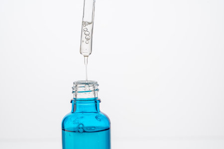Dropper with a drop of hyaluronic acid and collagen serum and a blue bottle on a white background. Close-up. Copyspace. High quality photoの写真素材