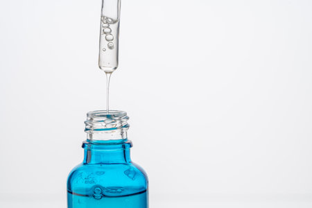 Dropper with a drop of hyaluronic acid and collagen serum and a blue bottle on a white background. Close-up. Copyspace. High quality photoの写真素材
