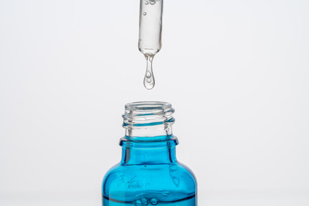 Dropper with a drop of hyaluronic acid and collagen serum and a blue bottle on a white background. Close-up. Copyspace. High quality photoの写真素材