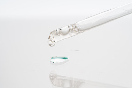 Dropper with collagen and hyaluronic acid serum on a white background with reflection. A drop of lotion for the skin of the face on the glass. Close-up, macro photography. copyspace. High quality photoの写真素材