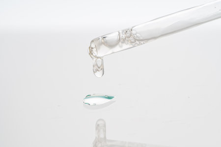 Dropper with collagen and hyaluronic acid serum on a white background with reflection. A drop of lotion for the skin of the face on the glass. Close-up, macro photography. copyspace. High quality photoの写真素材