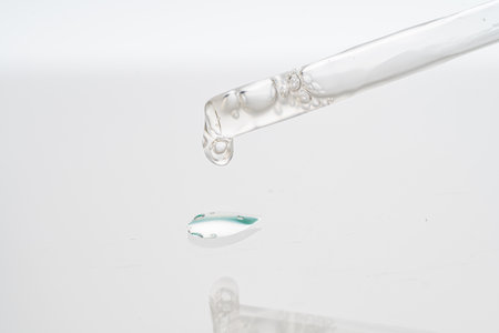 Dropper with collagen and hyaluronic acid serum on a white background with reflection. A drop of lotion for the skin of the face on the glass. Close-up, macro photography. copyspace. High quality photoの写真素材