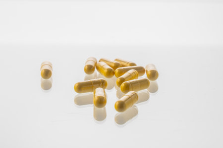 Yellow pills are scattered on a white background with a reflective surface. High quality photoの写真素材