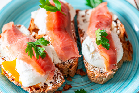 Poached eggs with salmon on bread toast with cream cheese on a turquoise plate. Close-up. A delicious and healthy family breakfast with omega. High quality photoの写真素材