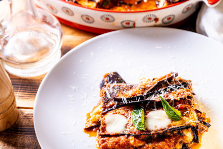 Eggplants alla parmesano on a white plate on a wooden table with a white napkin. Baked eggplants with tomatoes and cheese according to a traditional Italian recipe. High quality photoの写真素材