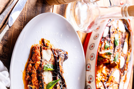 Eggplants alla parmesano on a white plate on a wooden table with a white napkin. Baked eggplants with tomatoes and cheese according to a traditional Italian recipe. High quality photoの写真素材