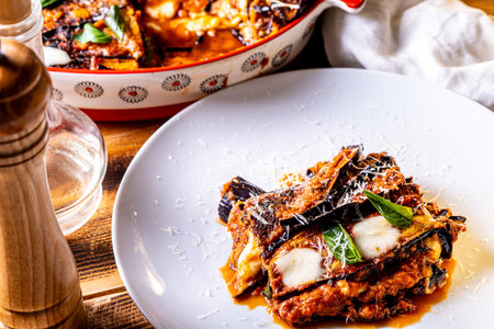 Eggplants alla parmesano on a white plate on a wooden table with a white napkin. Baked eggplants with tomatoes and cheese according to a traditional Italian recipe. High quality photoの写真素材