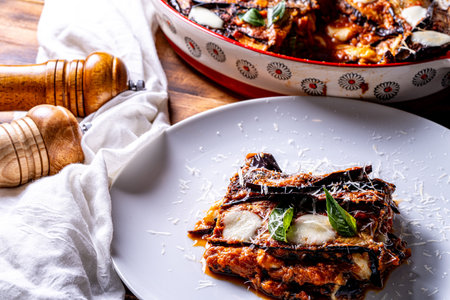 Eggplants alla parmesano on a white plate on a wooden table with a white napkin. Baked eggplants with tomatoes and cheese according to a traditional Italian recipe. High quality photoの写真素材