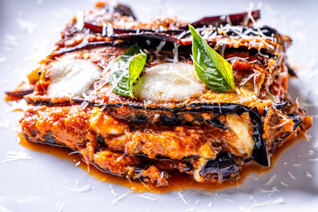 Eggplants alla parmesano on a white plate on a wooden table with a white napkin. Baked eggplants with tomatoes and cheese according to a traditional Italian recipe. Close-up. High quality photoの写真素材