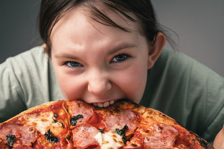 A little girl takes a bite out of a large pizza. Little girl bites into pizza and looks close-up at the frame. High quality photoの写真素材