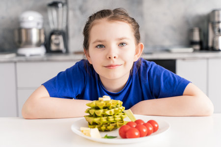 Portrait of a happy little girl having breakfast in the kitchen at home. Healthy breakfast of waffles with spinach, cheese and tomatoes. Selected focus.の写真素材