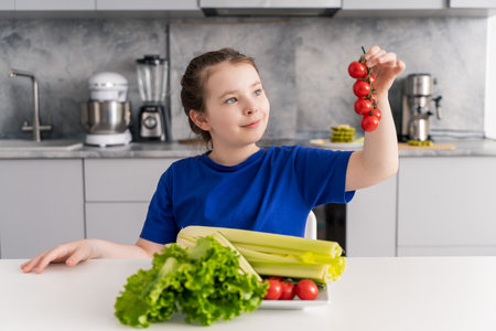 Cute little pre-teen girl looking at a sprig of tomatoes sitting in the kitchen at home in front of a plate of vegetables and salad. Selected focus. High quality photoの写真素材