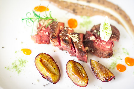 Medium-rare steak, sliced, with dogwood sauce on a white plate with roasted plums and rosemary cream cheese dumplings. Top view. High quality photoの写真素材