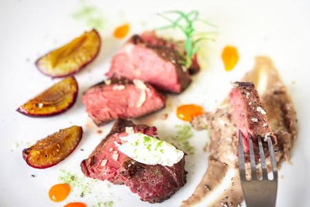 Medium-rare steak, sliced, with dogwood sauce on a white plate with roasted plums and rosemary cream cheese dumplings. Top view. High quality photoの写真素材