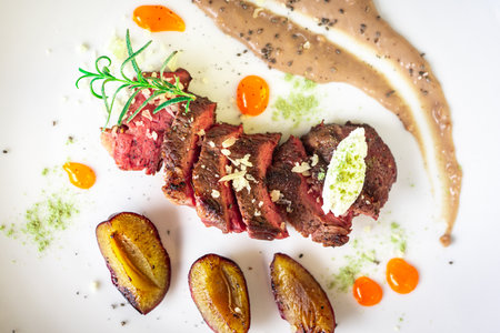 Medium-rare steak, sliced, with dogwood sauce on a white plate with roasted plums and rosemary cream cheese dumplings. Top view. High quality photoの写真素材