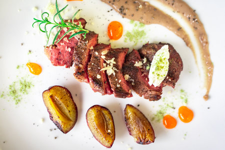 Medium-rare steak, sliced, with dogwood sauce on a white plate with roasted plums and rosemary cream cheese dumplings. Top view. High quality photoの写真素材